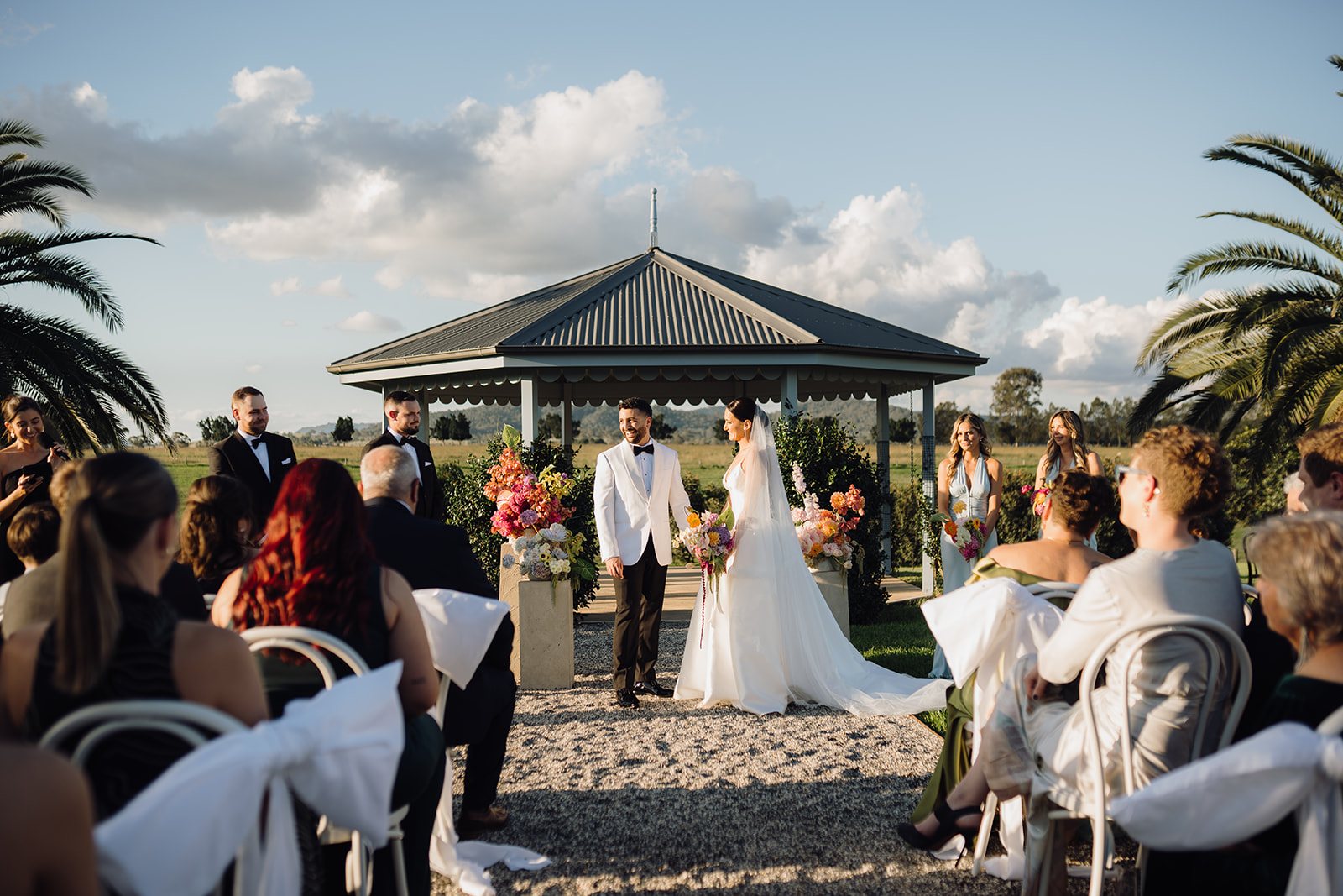 A ceremony at the gazebo with palms, guests seated, the couple at the altar