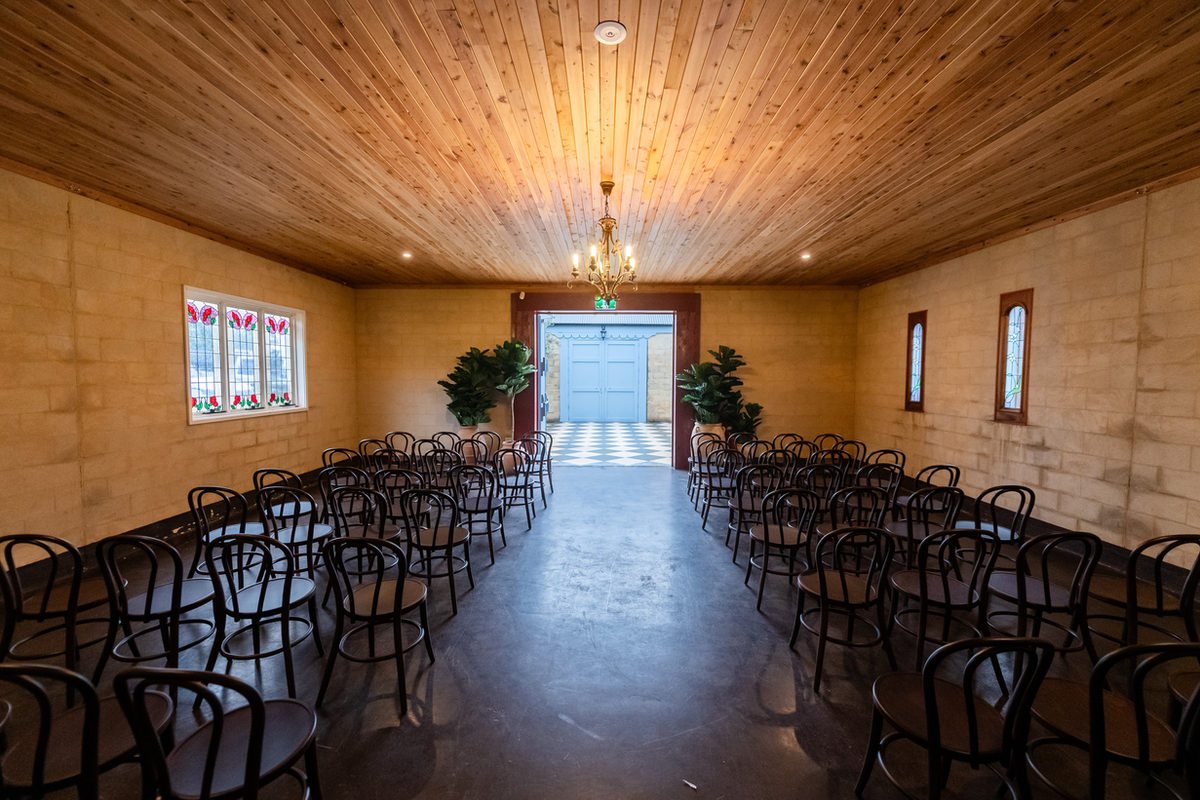 The Indoor Chapel: rows of bentwood chairs in the timber-lined hall facing the blue door