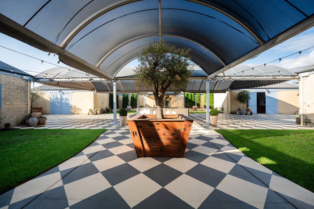 The Piazza: curved roof, checkerboard floor, olive tree and marble bar